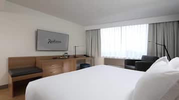 A hotel room with a large bed, a desk with a coffee maker, a chair, and a TV mounted on the wall.