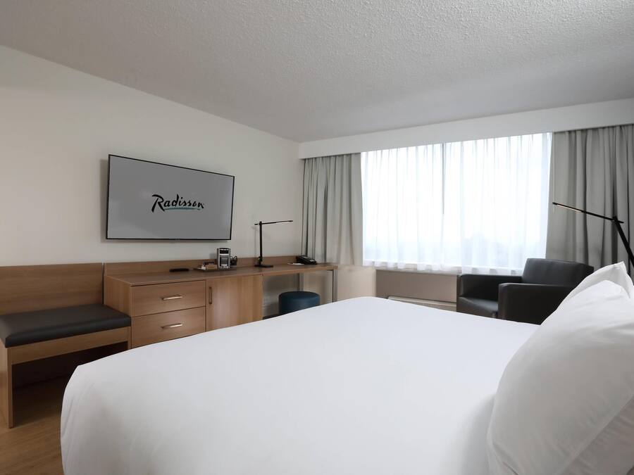 A hotel room with a large bed, a desk with a coffee maker, a chair, and a TV mounted on the wall.