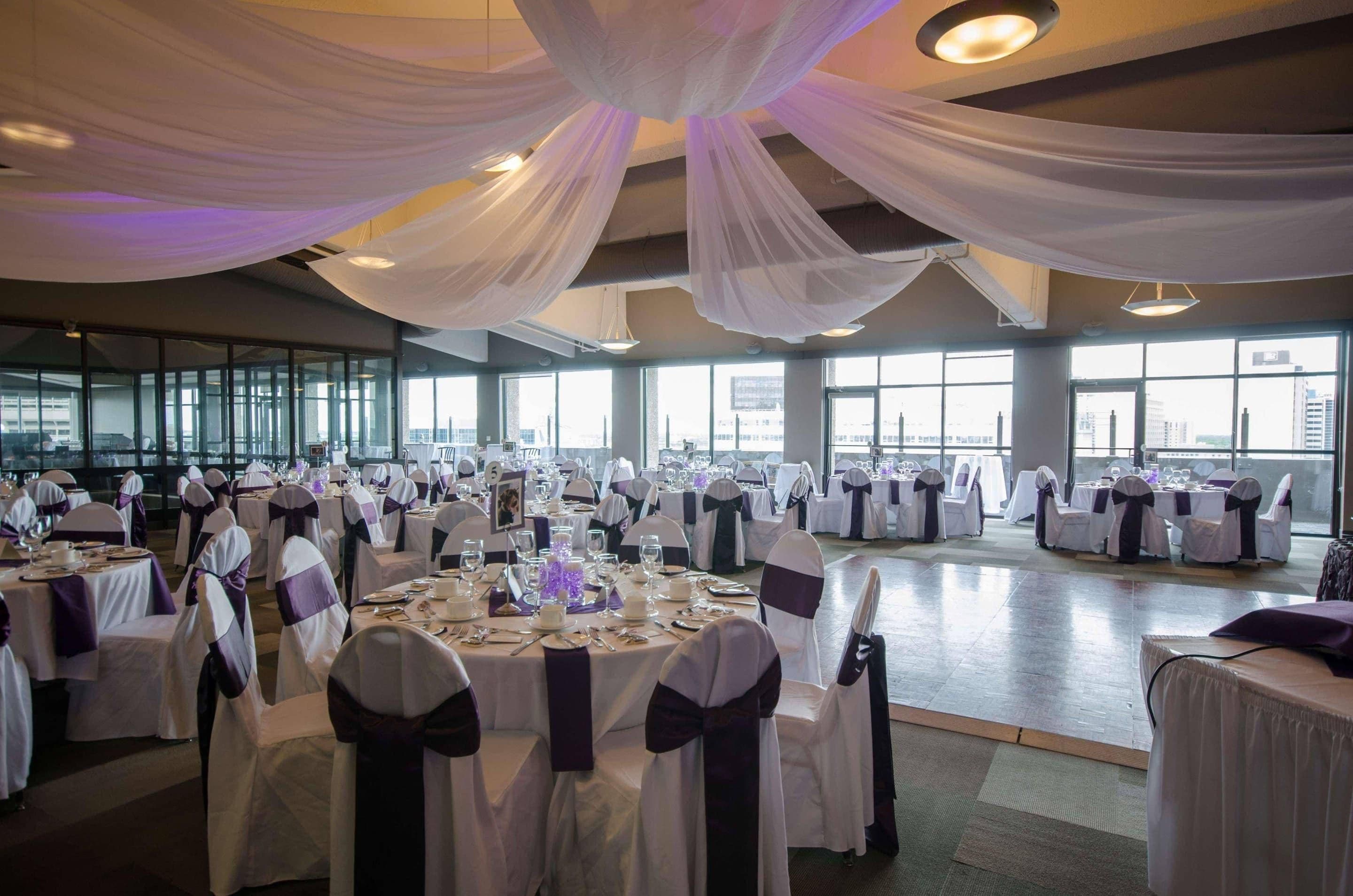 Un salón de banquetes con mesas redondas, manteles blancos y sillas con cintas.