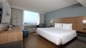 Habitación de hotel con una cama grande, un escritorio, una silla, una lámpara y vistas a la ciudad.
