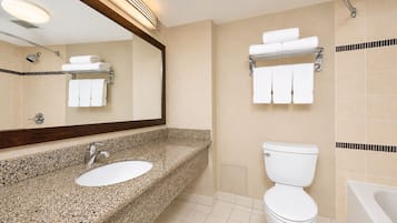 Un baño moderno con lavamanos de granito, inodoro, bañera y toallero con toallas dobladas.