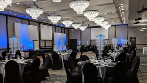 Un salón de banquetes con varias mesas redondas, sillas negras y grandes candelabros.