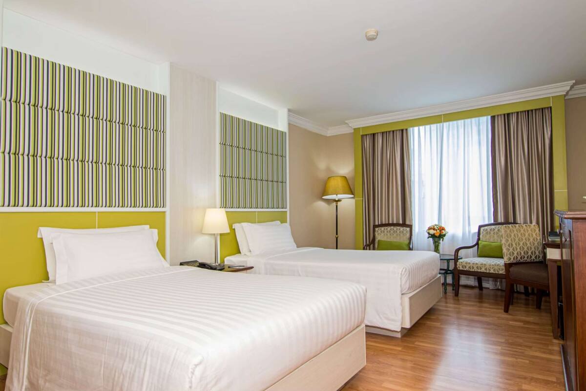 A hotel room with two beds, a desk, a chair, and a window with curtains.