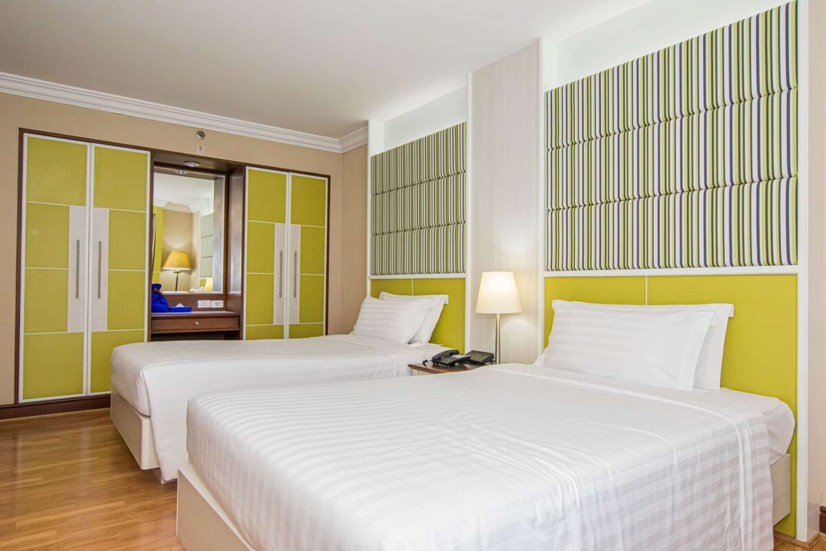 Habitación de hotel con dos camas, un armario, un espejo y un papel tapiz estampado.