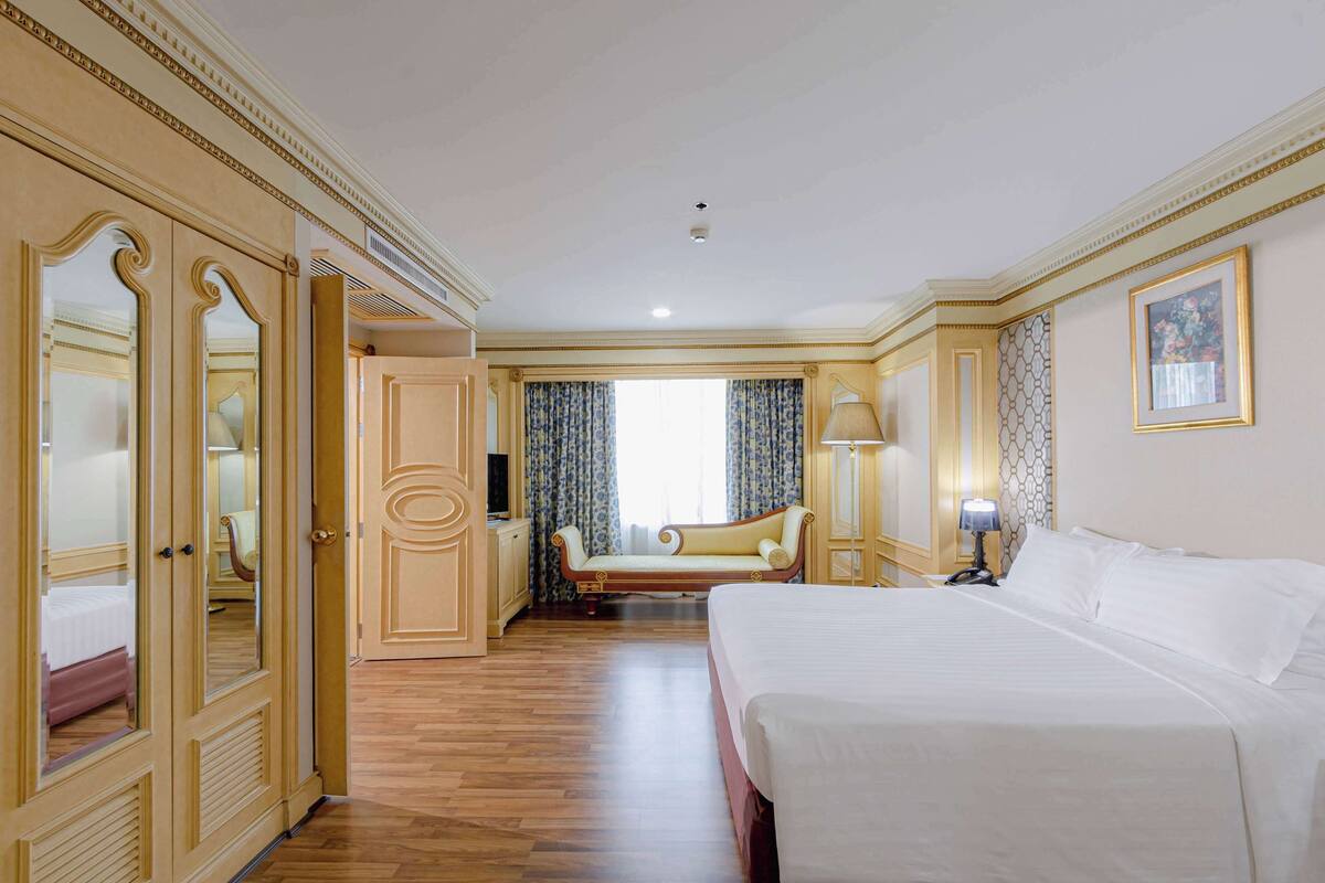 A hotel room with a large bed, a seating area with a sofa, and a wardrobe with mirrors.