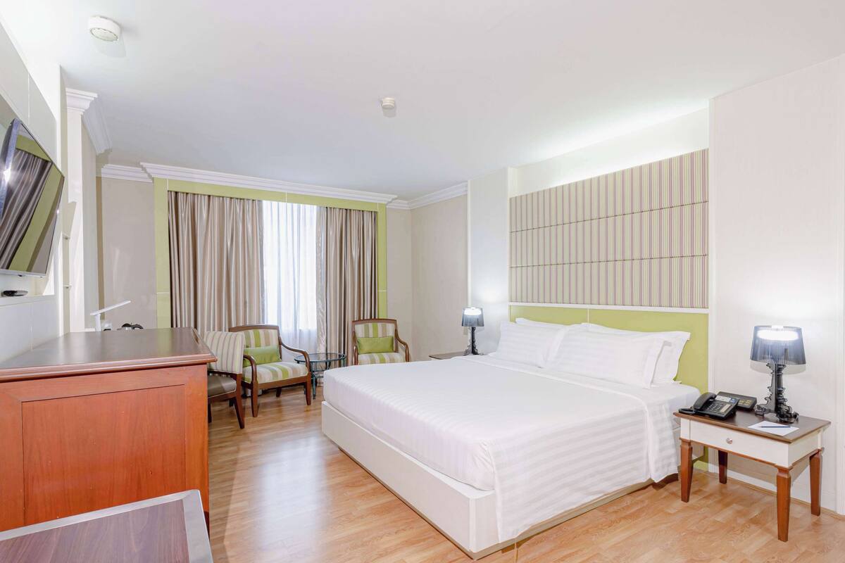 A hotel room with a bed, bedside table, lamp, chair, and a television.