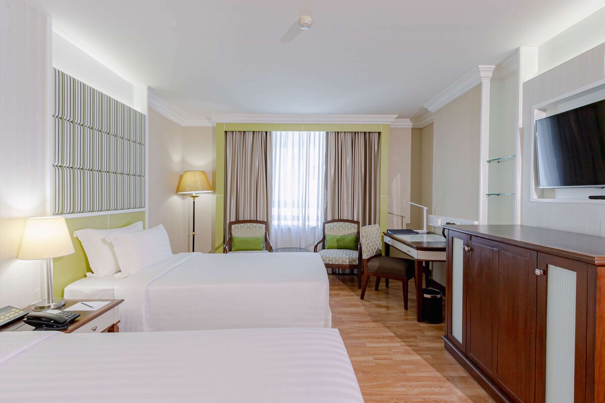 Una habitación de hotel con dos camas, un escritorio, sillas, un televisor y una lámpara.