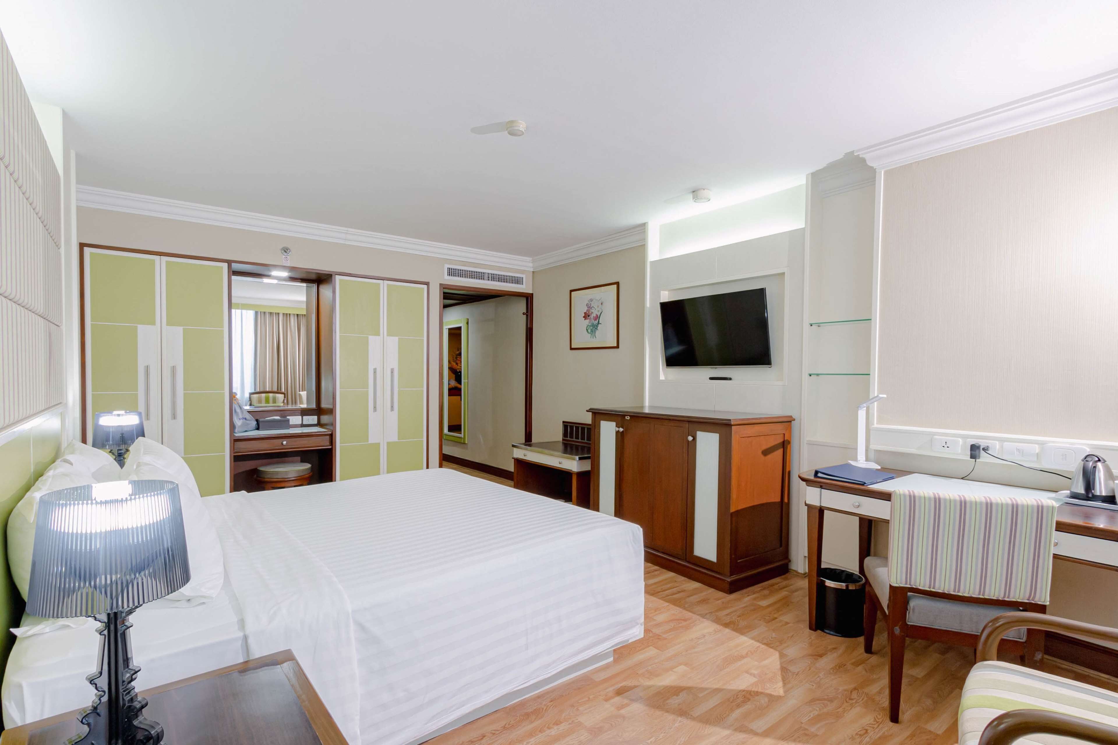 A hotel room with a bed, a desk, a television, a wardrobe, and a mirror.