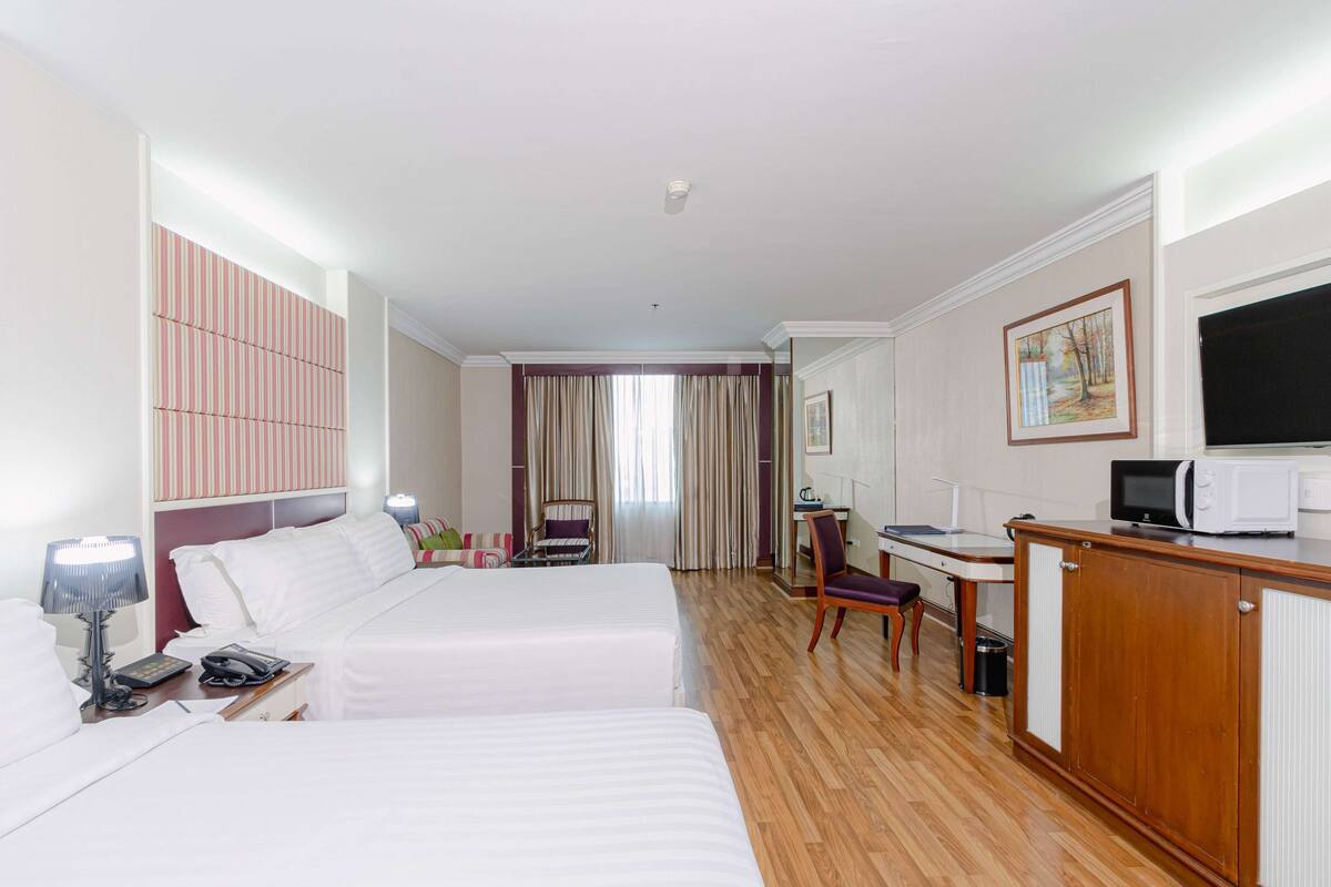 A hotel room with two beds, a desk, a television, and a microwave.
