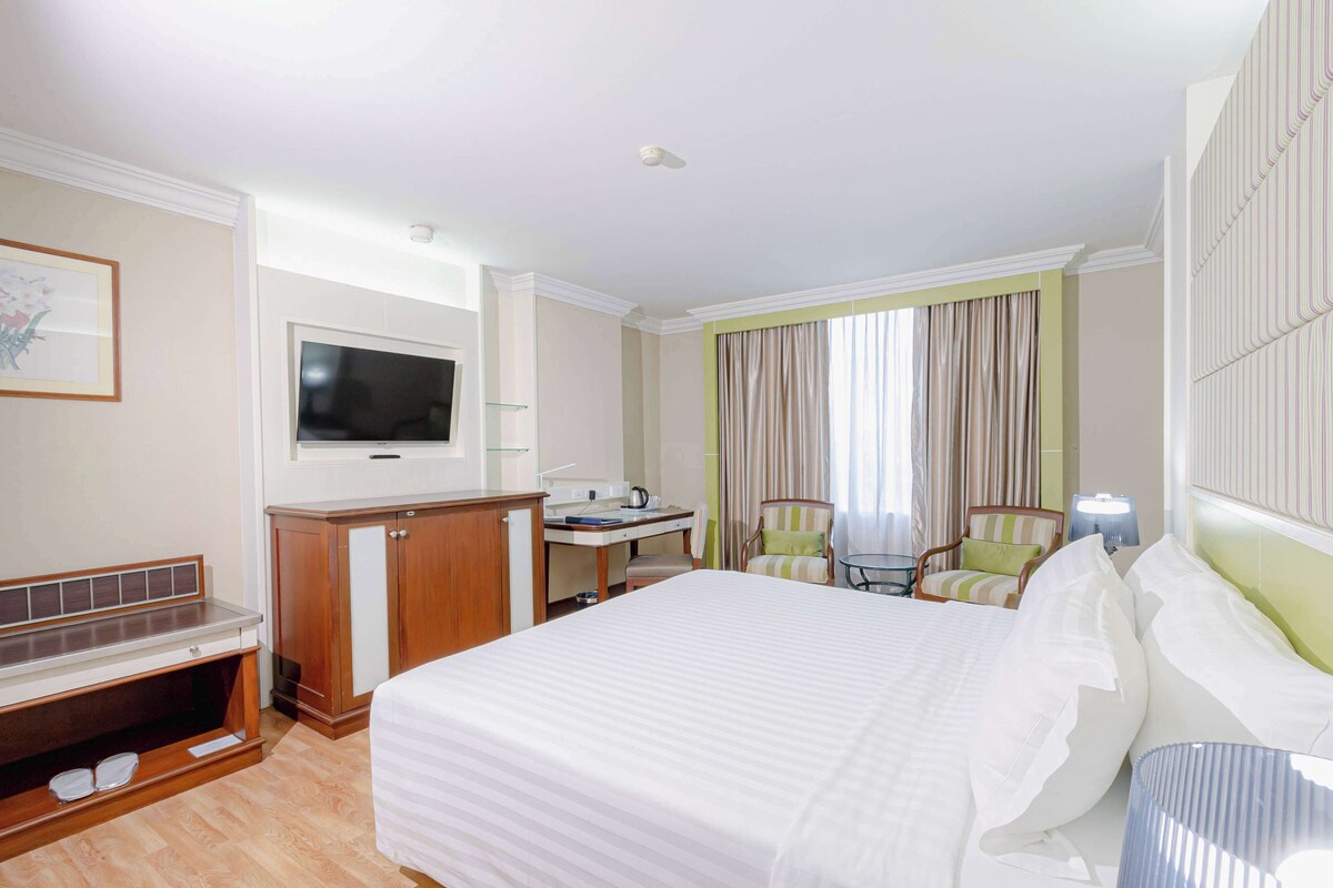 Una habitación de hotel con una cama grande, un escritorio con silla, televisión y una ventana con cortinas.