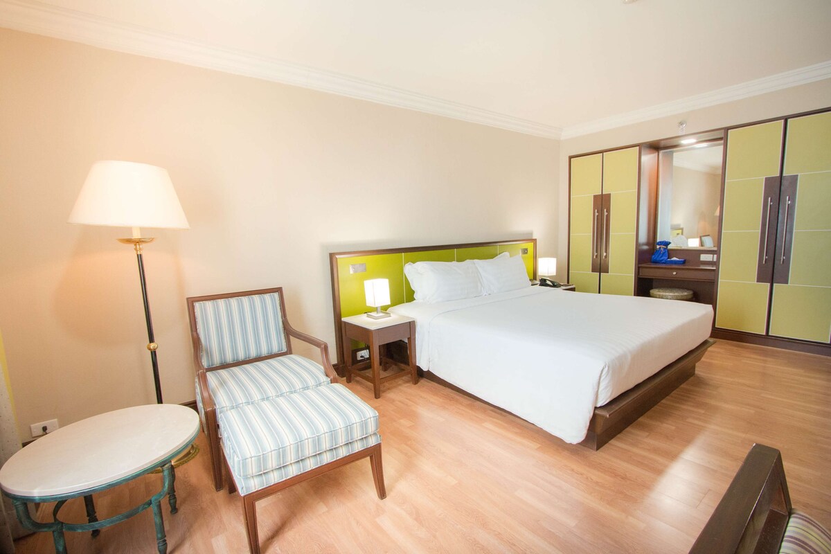 Una habitación de hotel con una cama, una silla, una mesa, una lámpara y un armario.