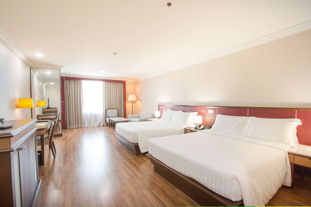 Habitación de hotel con dos camas, un escritorio con lámpara, una silla y una ventana con cortinas.