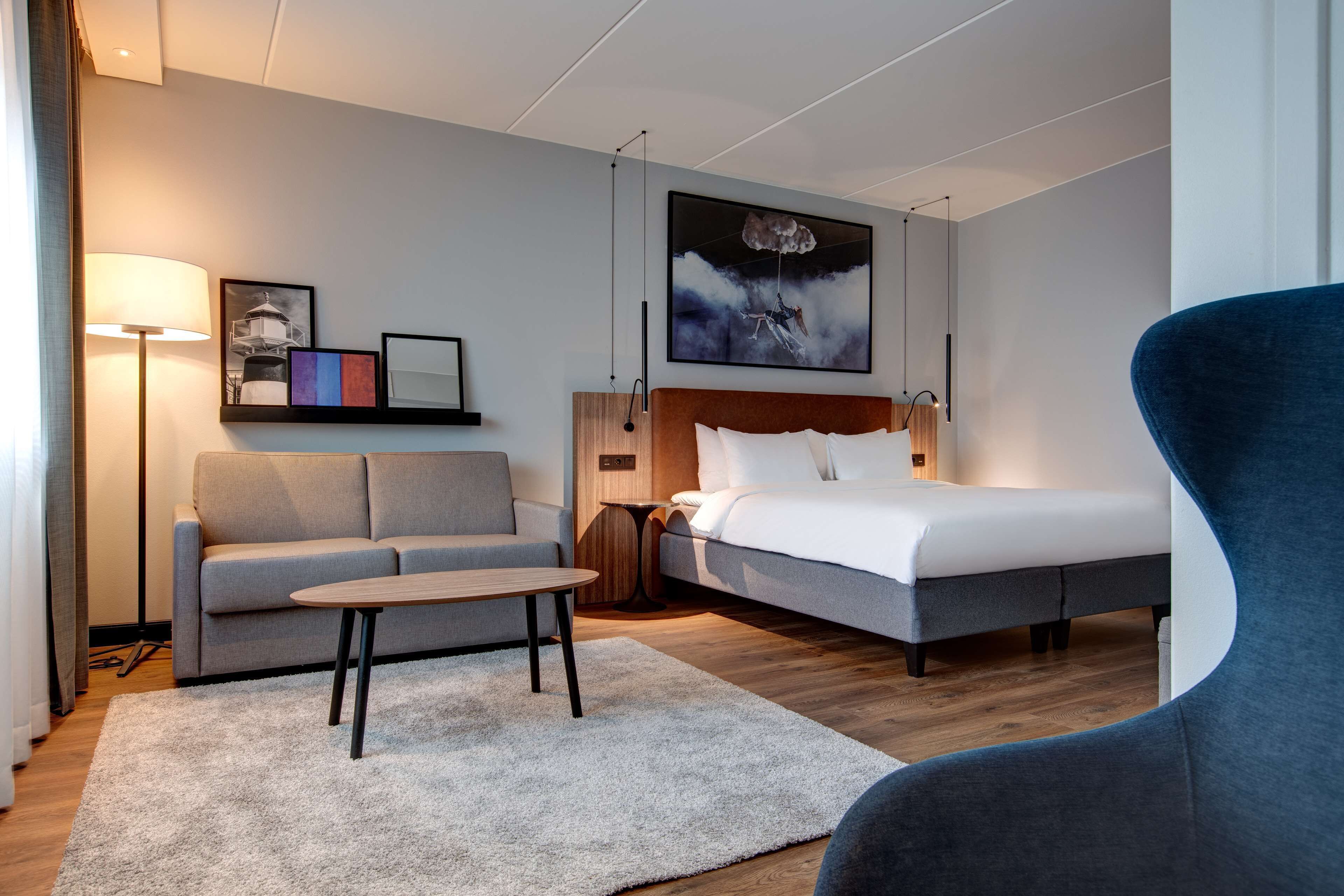 A modern hotel room with a bed, sofa, and a small table.