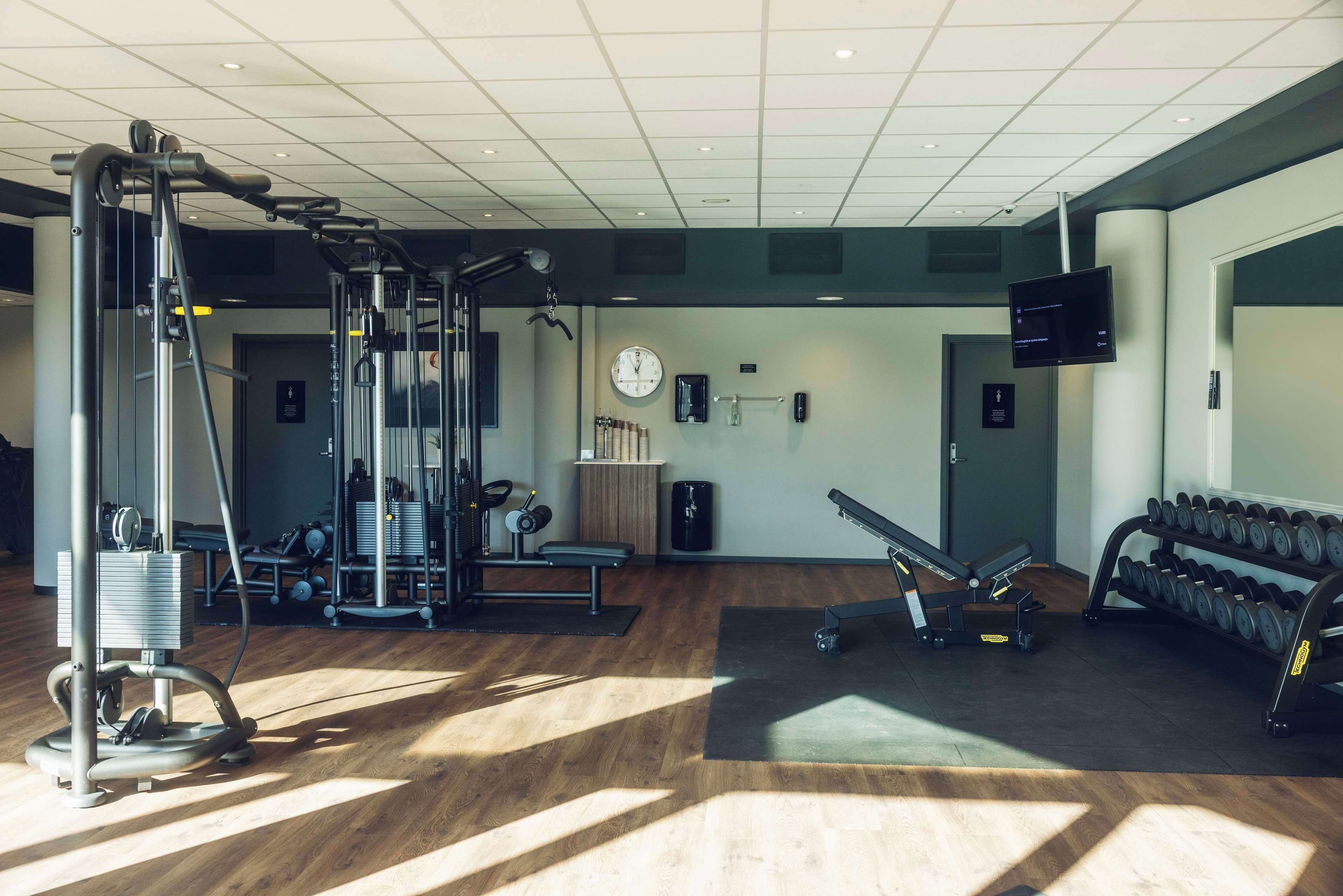 A gym with exercise equipment, a clock, and a TV on the wall.