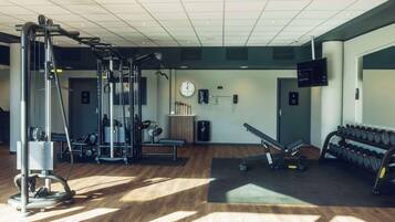A gym with exercise equipment, a clock, and a TV on the wall.