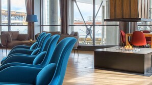 A modern lounge area with blue chairs, a central fire feature, and large windows offering views of the cityscape. - Radisson Blu Airport Hotel, Oslo Gardermoen (Ullensaker)