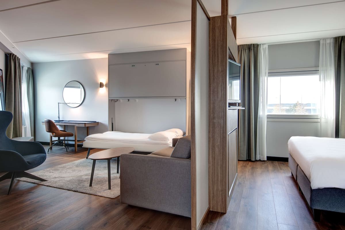 A modern hotel room with a bed, a sofa, a desk, and a TV.