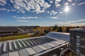 A modern building with a unique curved roof design, a parking area, and a view of a forested area in the background. - Radisson Blu Airport Hotel, Oslo Gardermoen (Ullensaker)