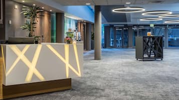 Un área de recepción moderna con mostrador, plantas en macetas y una pantalla digital.