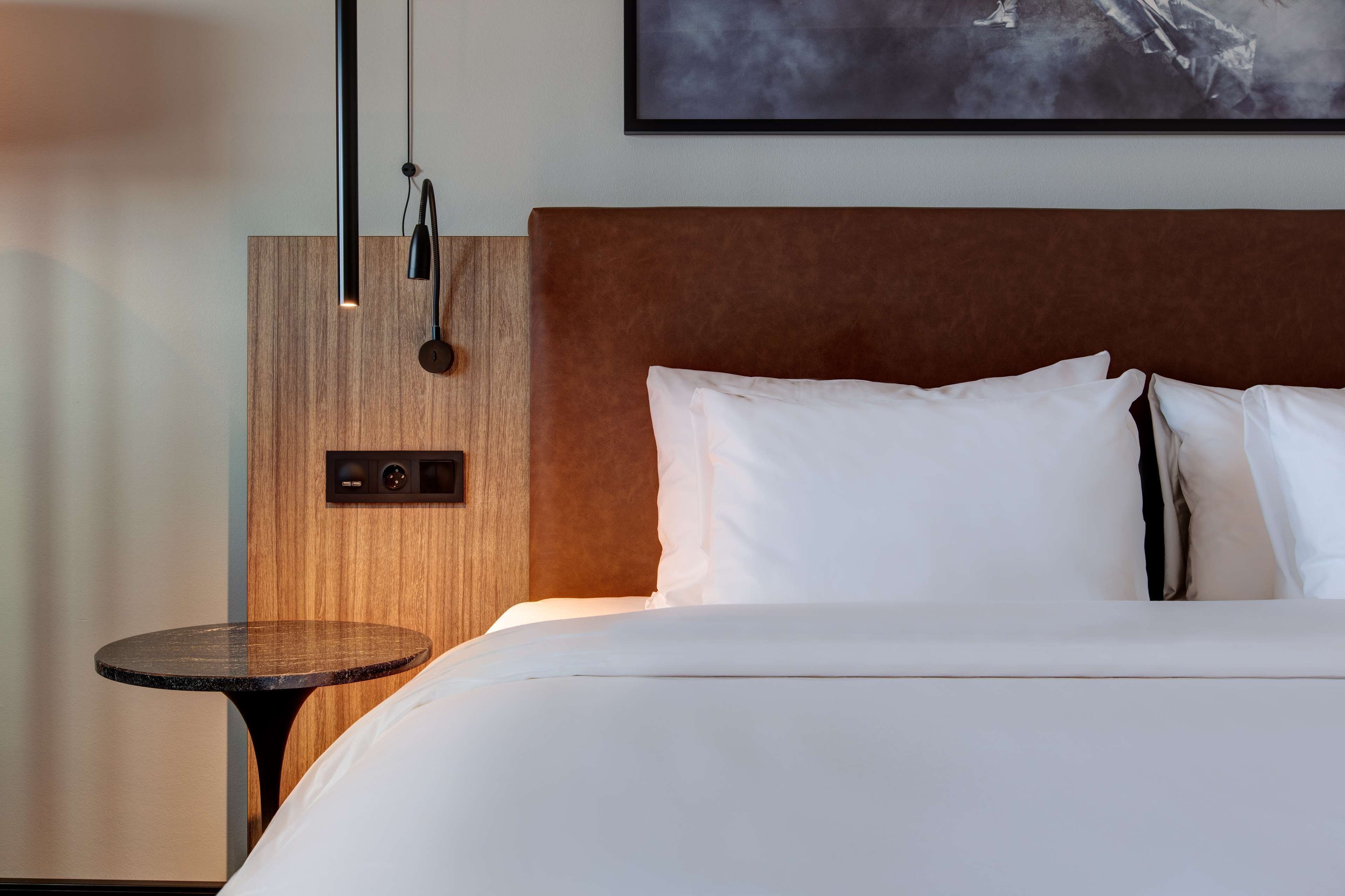 Ett hotellrum med en säng, ett runt bord och en väggmonterad lampa.