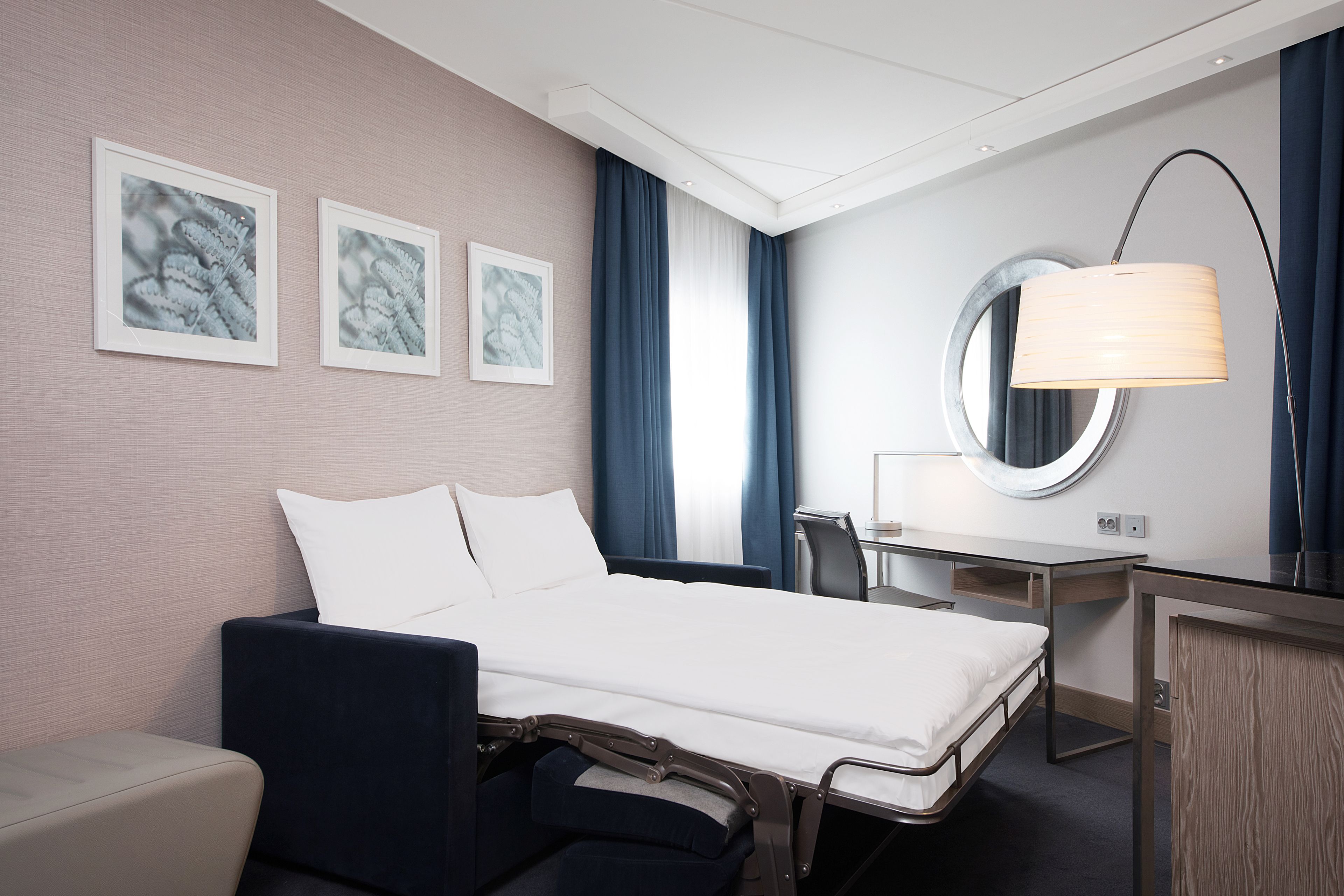 Une chambre d’hôtel avec un lit, un bureau, une chaise et un miroir rond.
