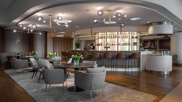 Un área de bar moderna con distribución curva, una mesa redonda central y taburetes de bar.