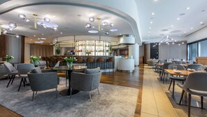 Un moderno vestíbulo de hotel con zona de bar, espacios para sentarse y un diseño de techo curvo.