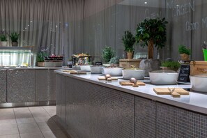 A modern kitchen counter with various food items and kitchenware, potted plants, and a chalkboard sign.