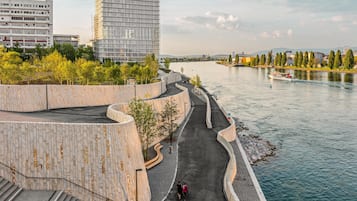 A riverside walkway with a curved stone wall, a boat on the water, and modern buildings in the background.