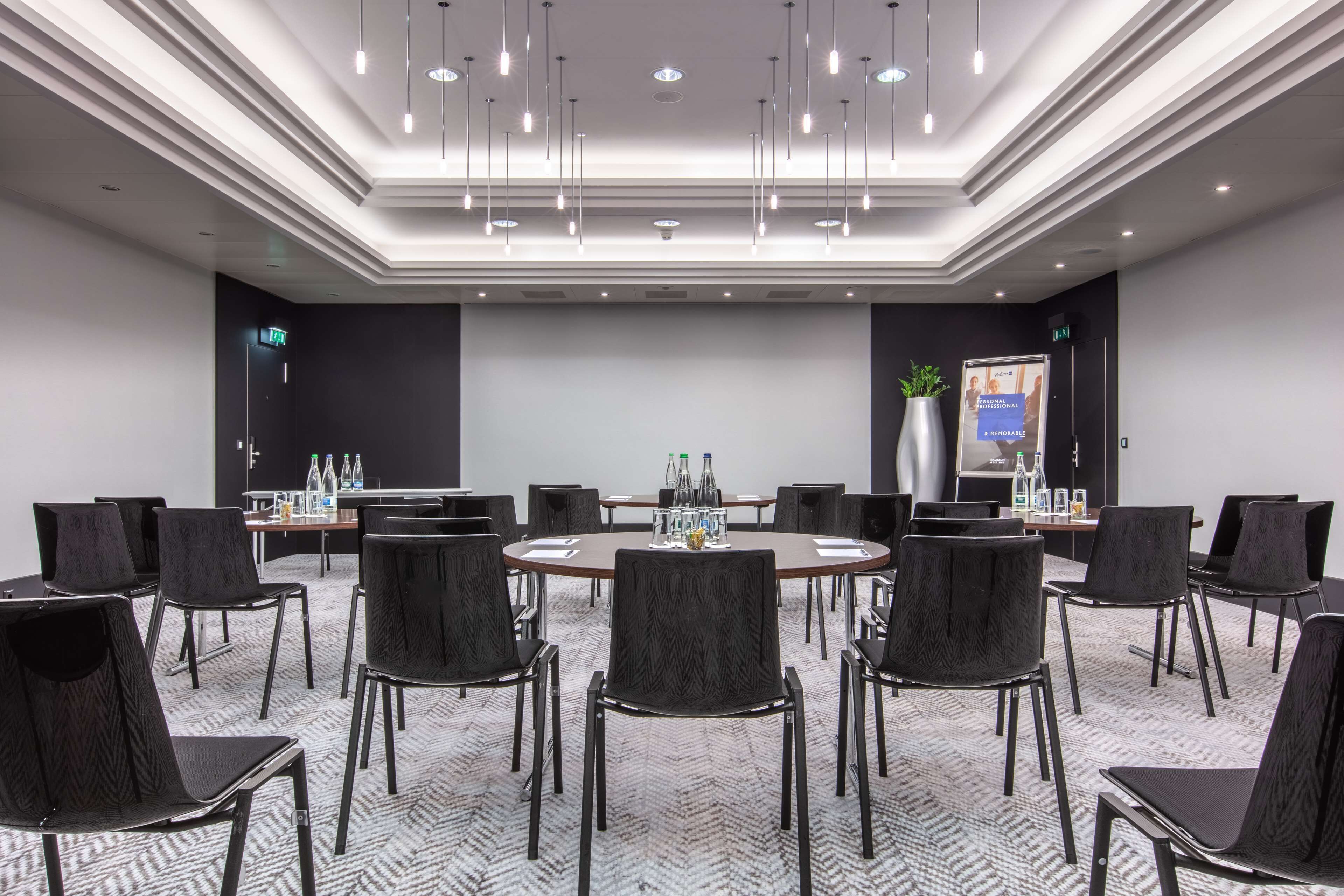 A conference room with a round table, black chairs, and a projector screen.