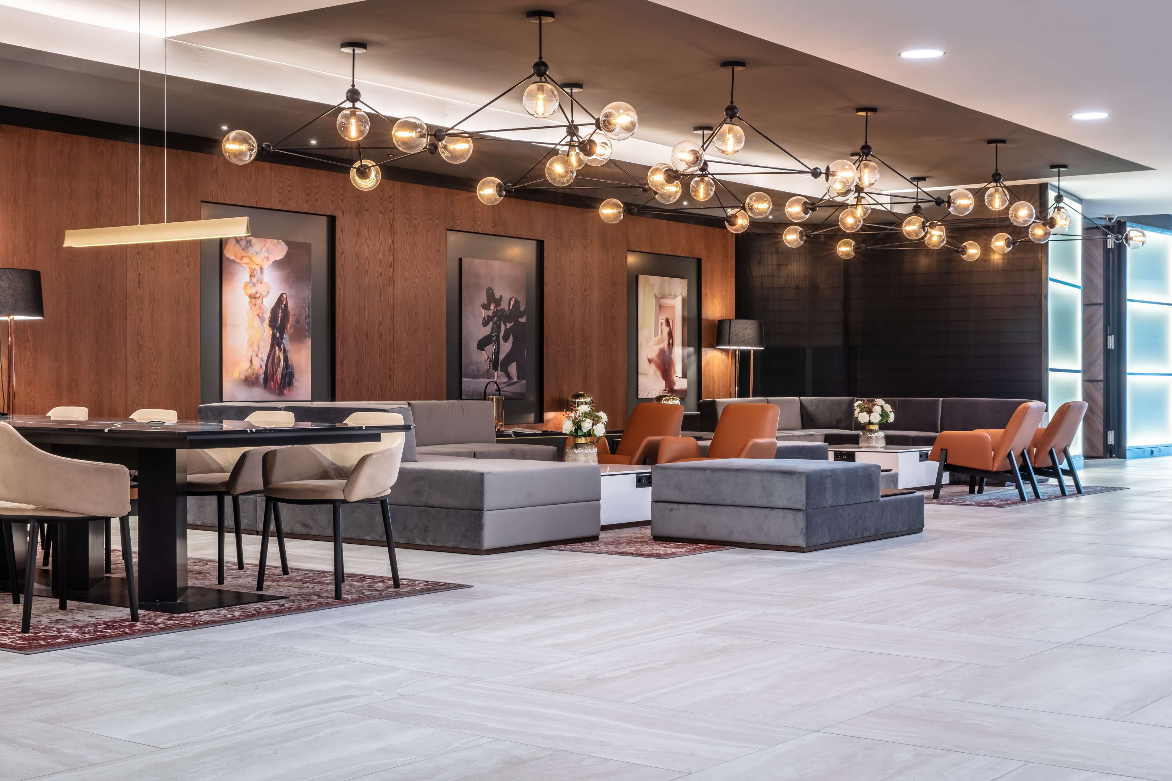 A modern hotel lobby with a dining area, seating arrangements, and a large chandelier.
