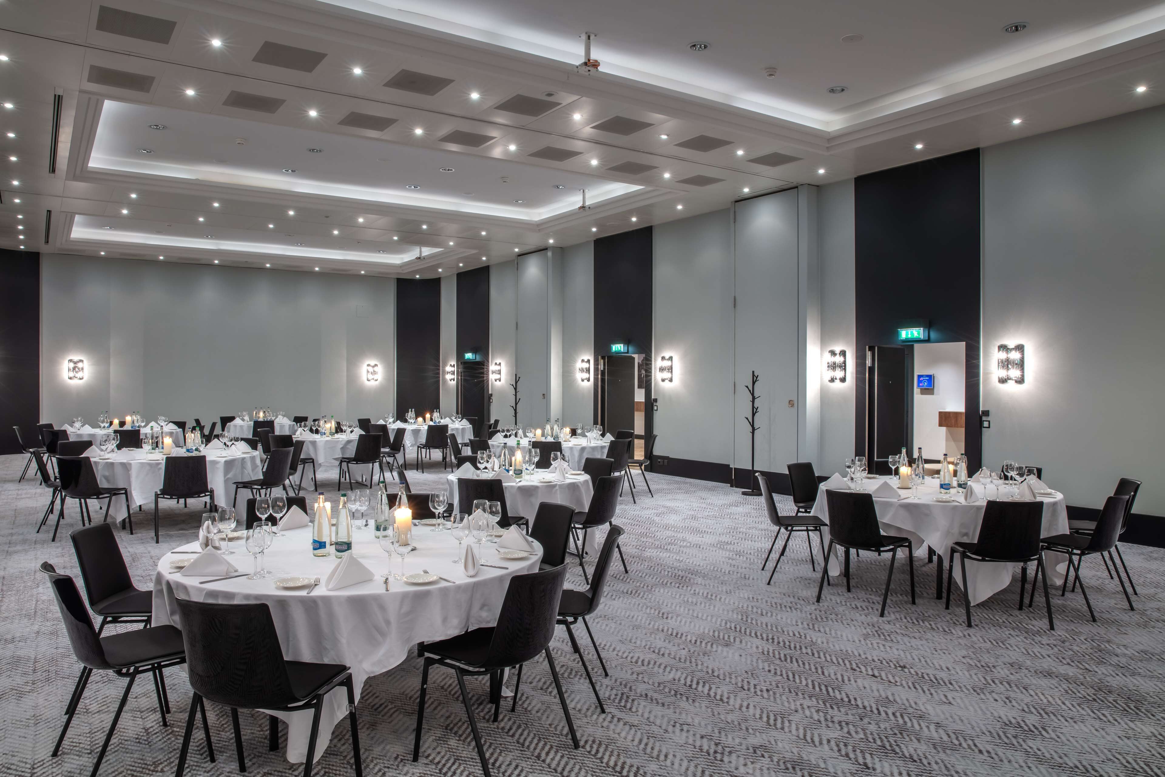 A large banquet hall with round tables set for dining, equipped with candles and table settings.