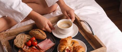 A breakfast tray with croissants, ham, bacon, tomatoes, and bread on a bed.