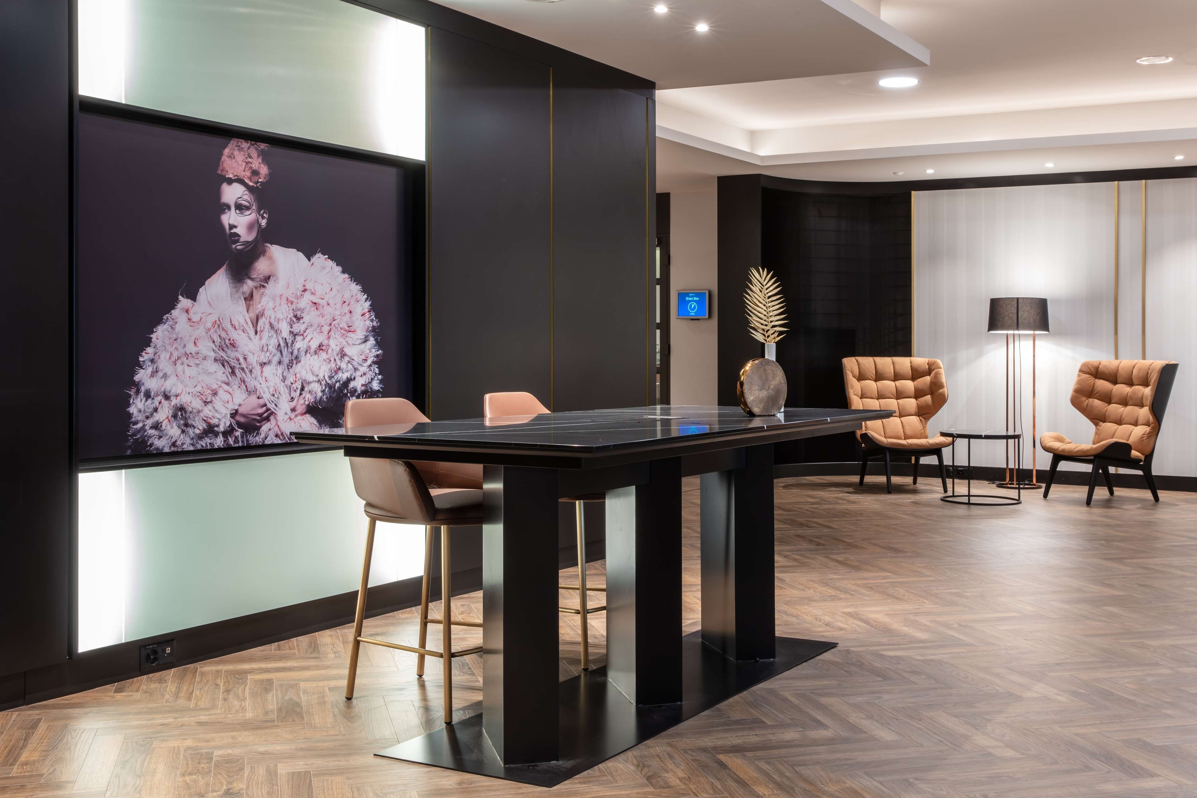 Een moderne vergaderruimte met een groot scherm waarop een portret staat, een zwarte tafel met stoelen en een decoratieve vaas.