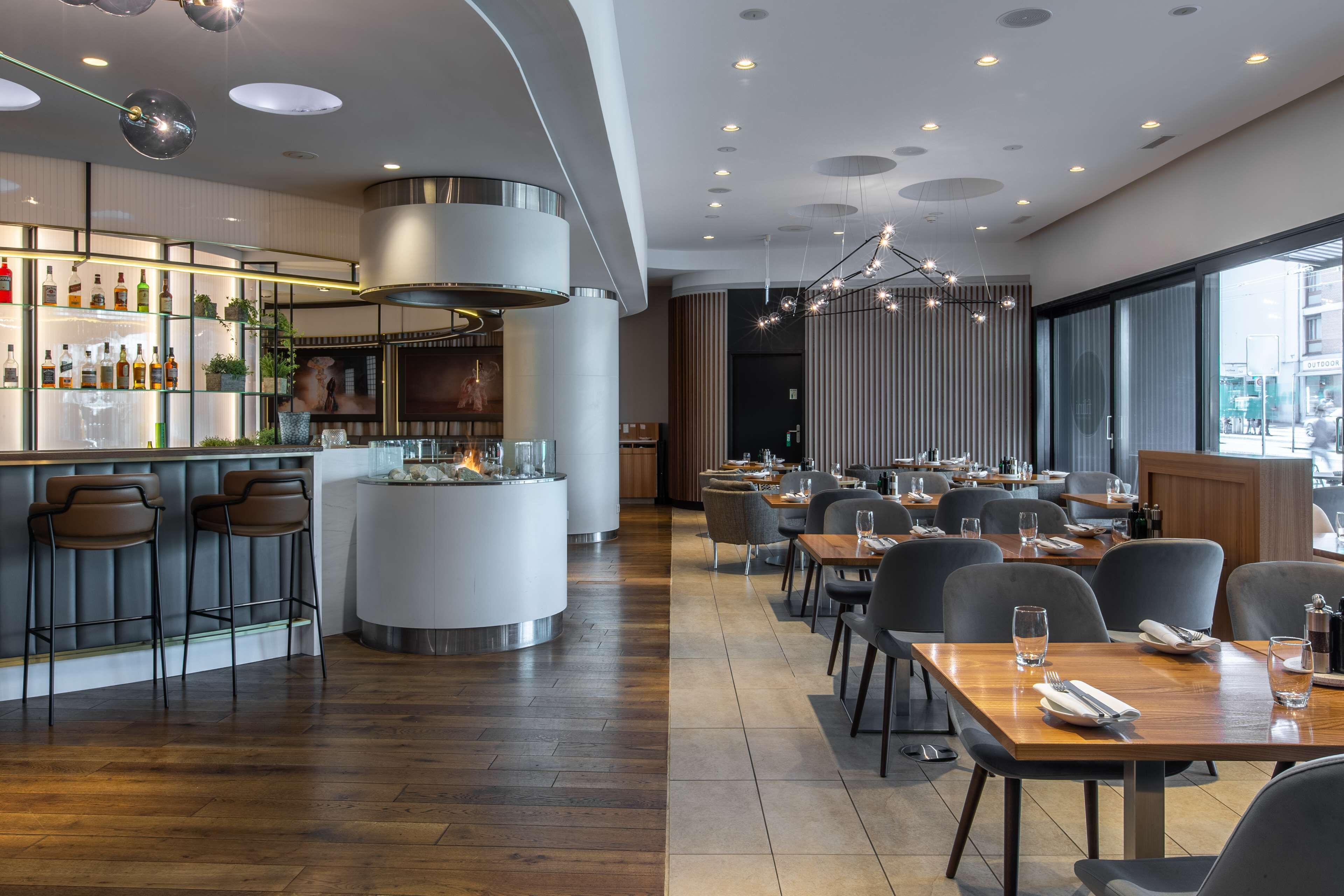 Un restaurante moderno con barra, mesas y un ventanal grande.