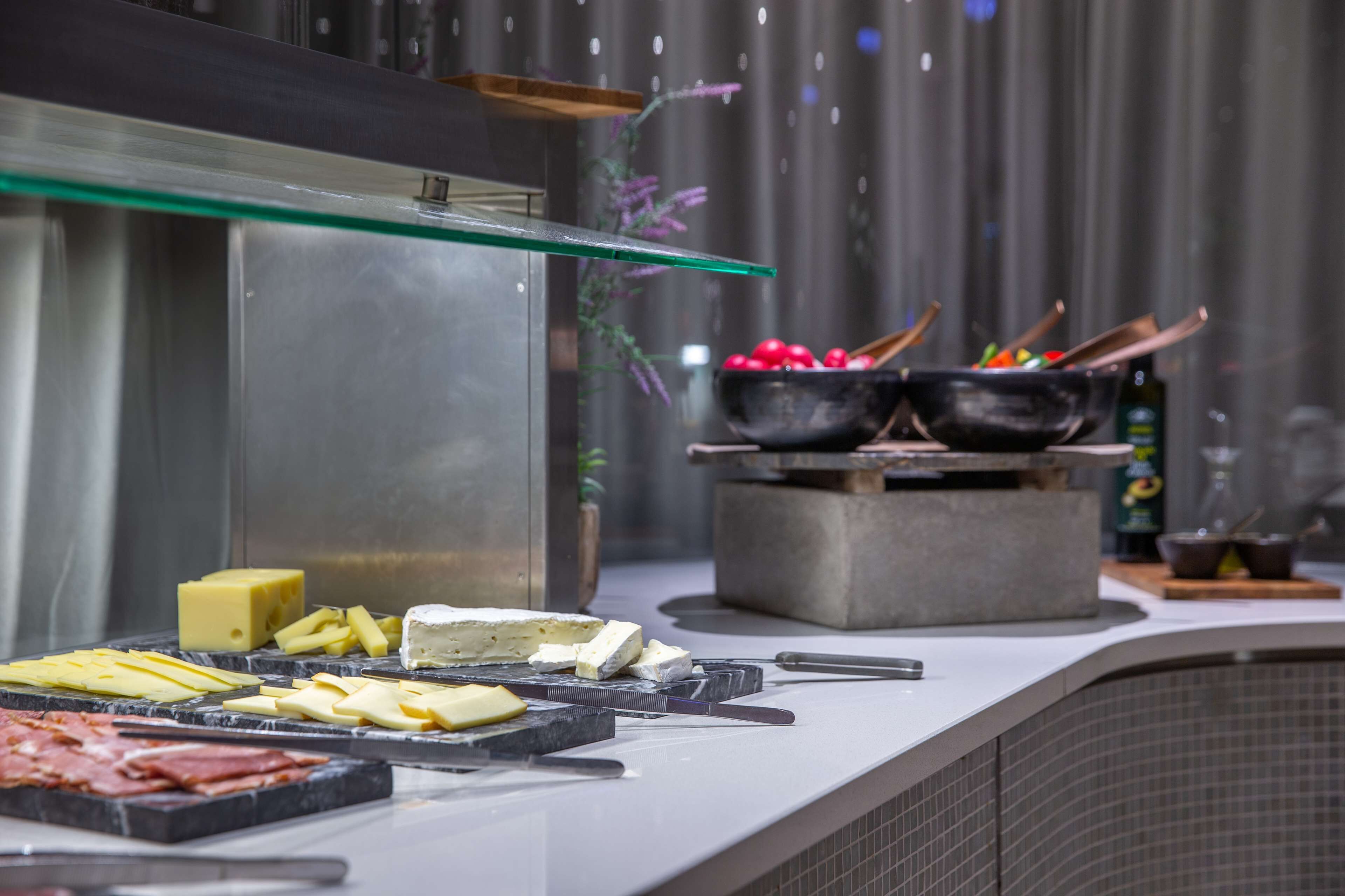 A buffet counter with various cheeses, meats, and cooking utensils.