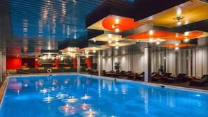 Una piscina con piso de baldosas, rodeada de sillas de descanso y una pared roja.