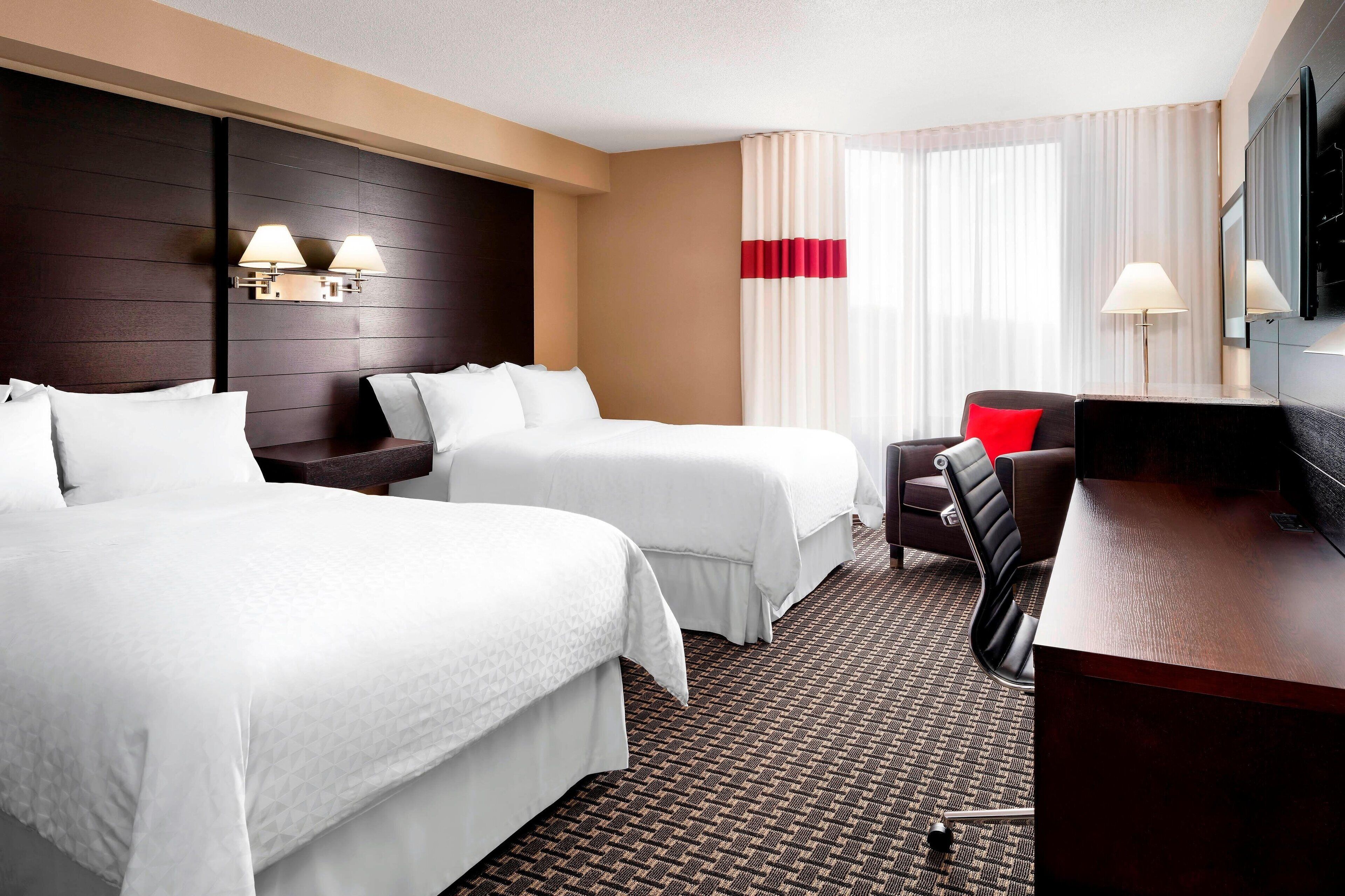 A hotel room with two beds, a desk, a chair, a TV, and a window with curtains.