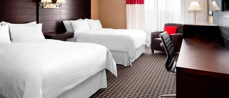 A hotel room with two beds, a desk, a chair, a TV, and a window with curtains.