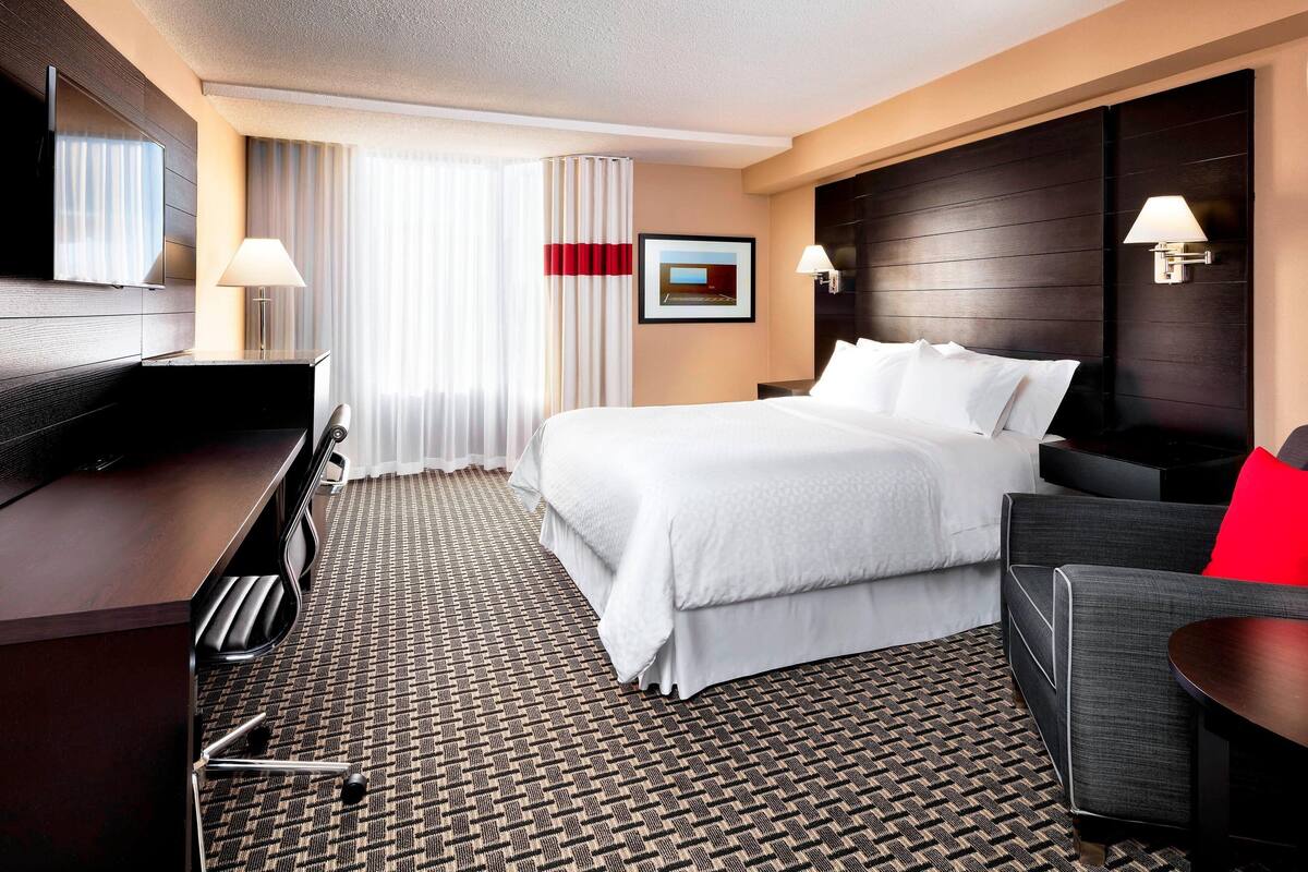 A hotel room with a bed, a desk, a chair, a TV, and a window with curtains.