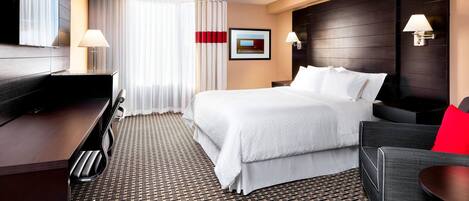 A hotel room with a bed, a desk, a chair, a TV, and a window with curtains.