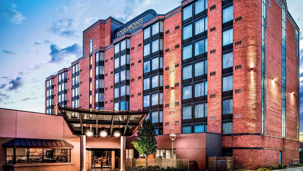 Un hotel de varios pisos con un llamativo letrero de 'Four Points by Sheraton', ventanas amplias y un área de entrada cubierta.