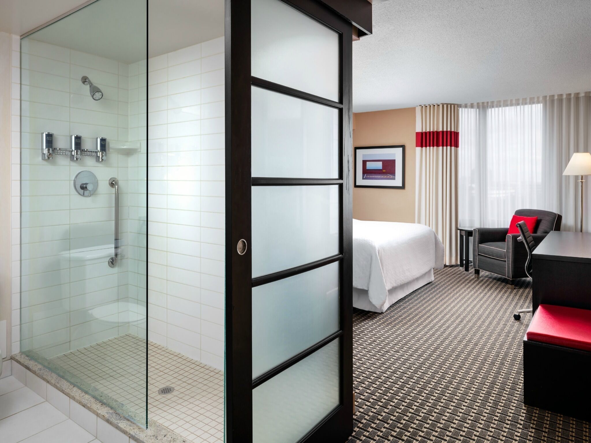 A hotel room with a glass shower enclosure, a bed, a desk, and a chair.