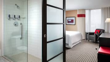 A hotel room with a glass shower enclosure, a bed, a desk, and a chair.