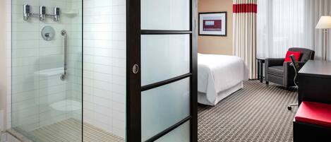A hotel room with a glass shower enclosure, a bed, a desk, and a chair.
