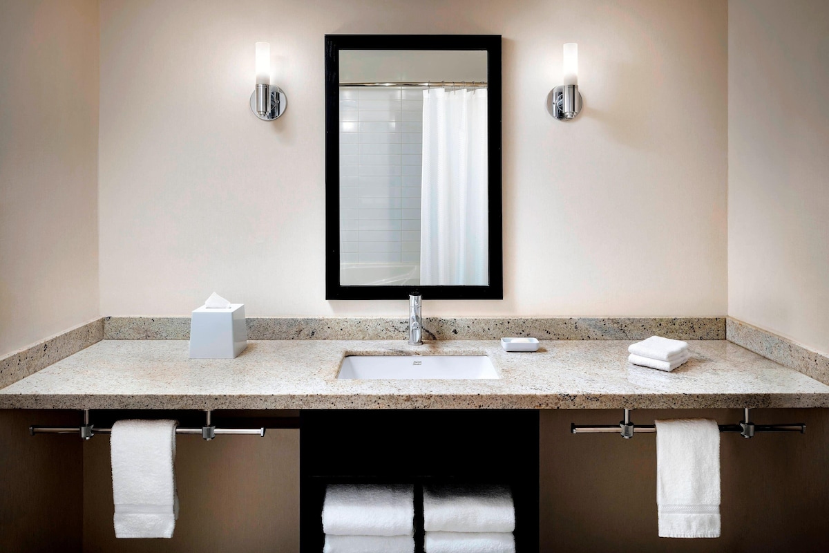 A bathroom with a granite countertop, a white sink, a mirror, and two towel racks with white towels.