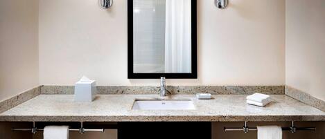 A bathroom with a granite countertop, a white sink, a mirror, and two towel racks with white towels.