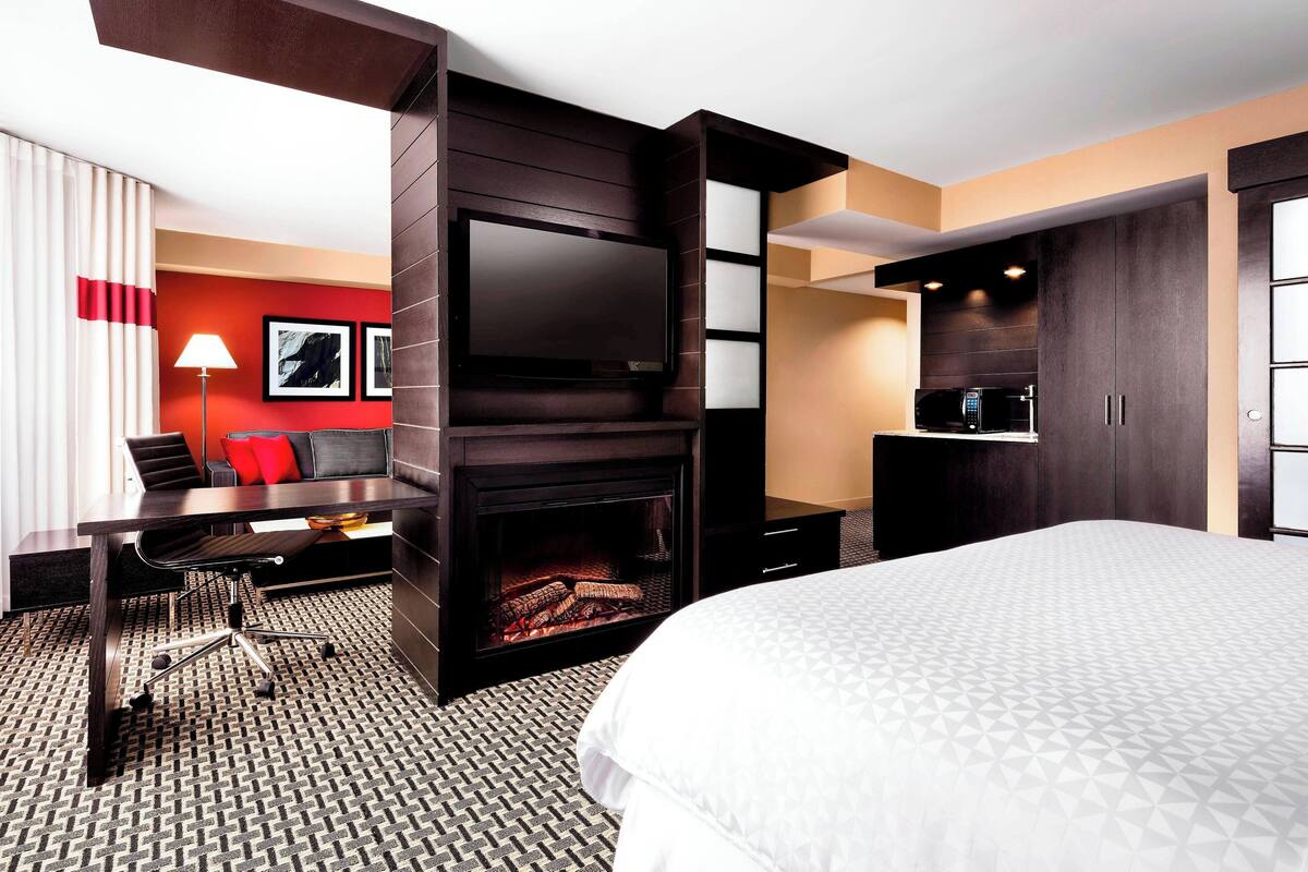 A hotel room with a large bed, a desk with a chair, a flat-screen TV, a fireplace, and a microwave.