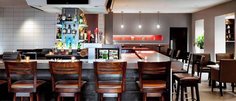 A modern bar area with a long counter, multiple bar stools, and a variety of bottles and glasses on shelves.