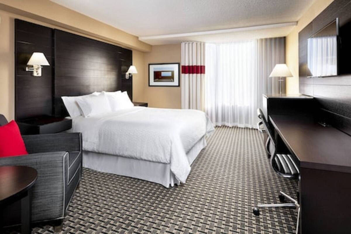 A hotel room with a large bed, a desk, a chair, a TV, and a window with curtains.
